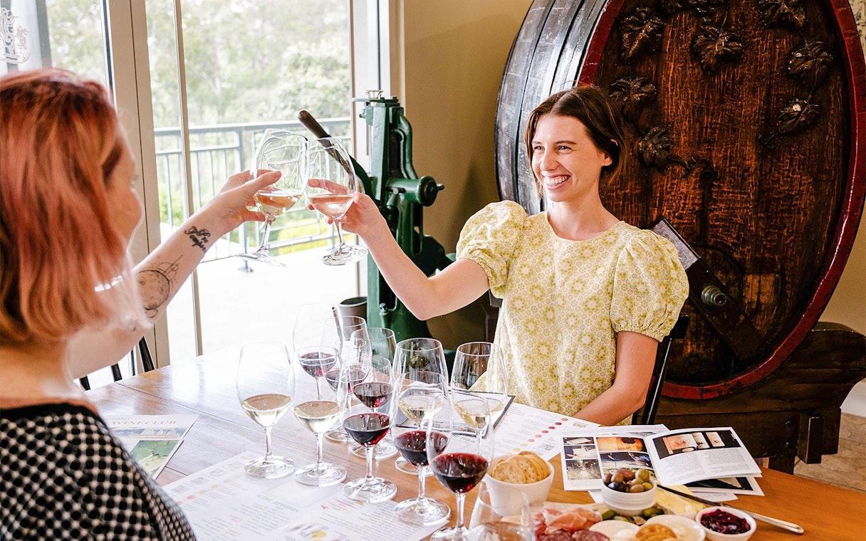 Friends toasting with wine glasses at a winery table with tasting menu.