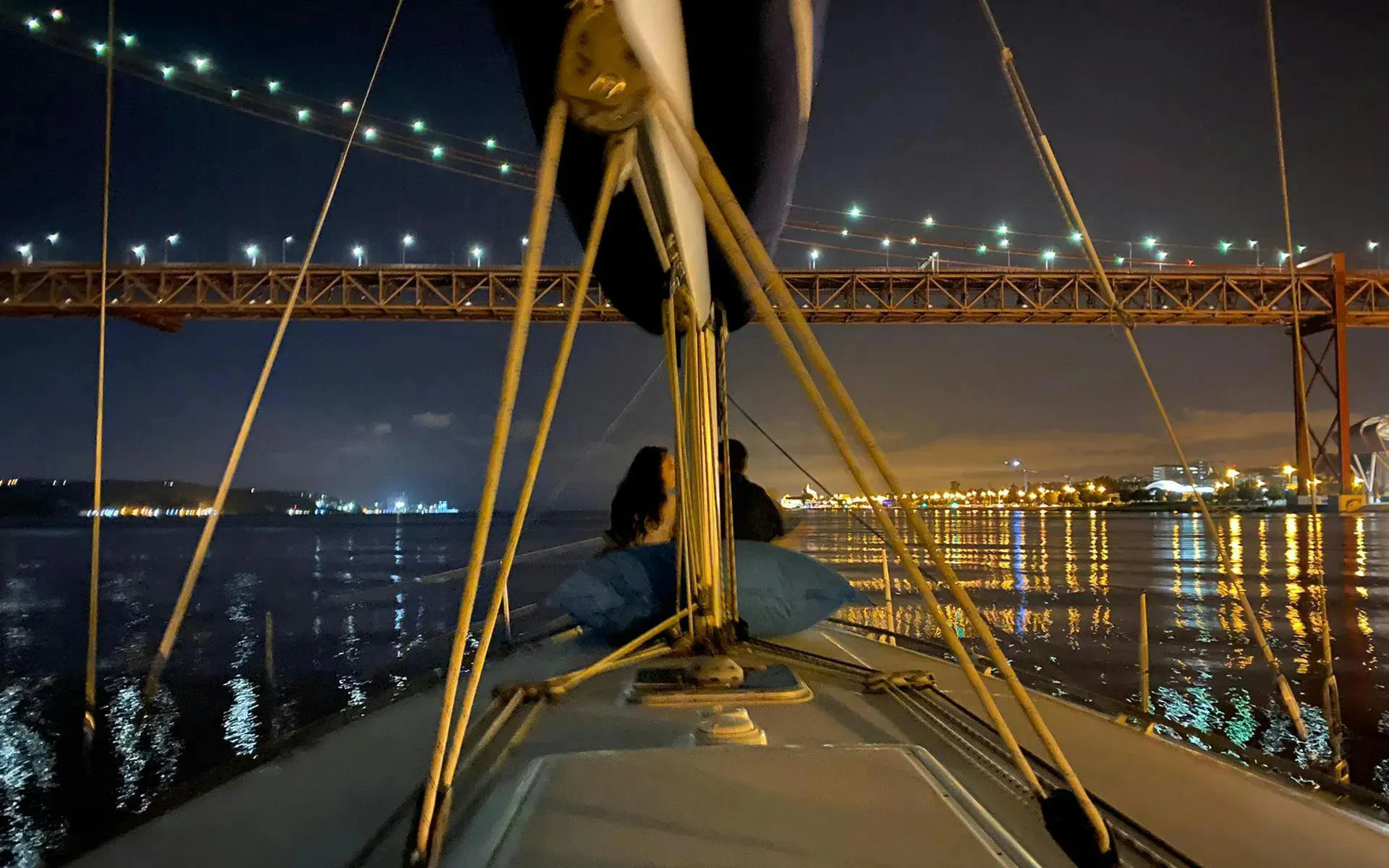 Couple enjoying Lisbon night cruise under illuminated bridge.