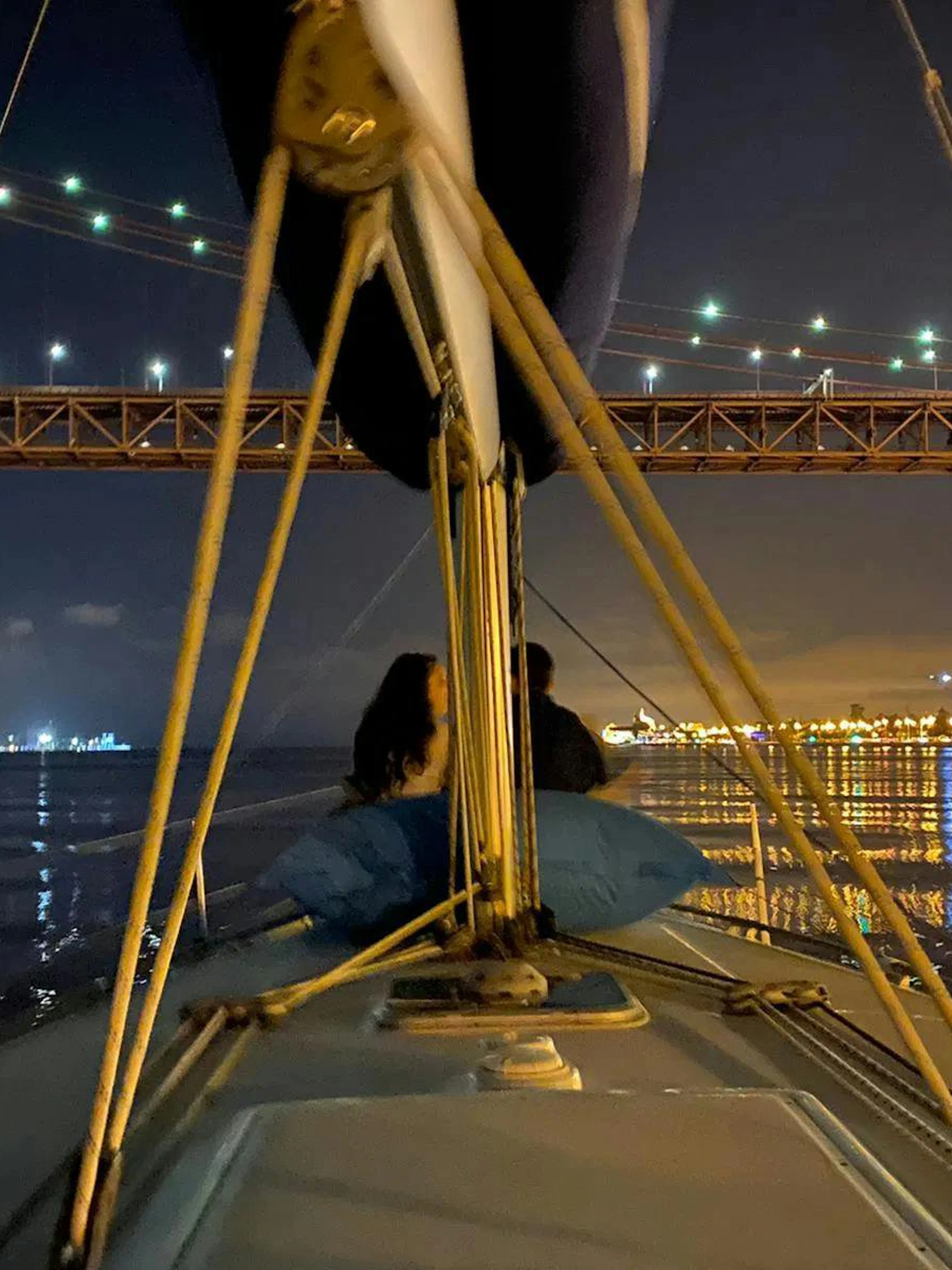 Couple enjoying Lisbon night cruise under illuminated bridge.