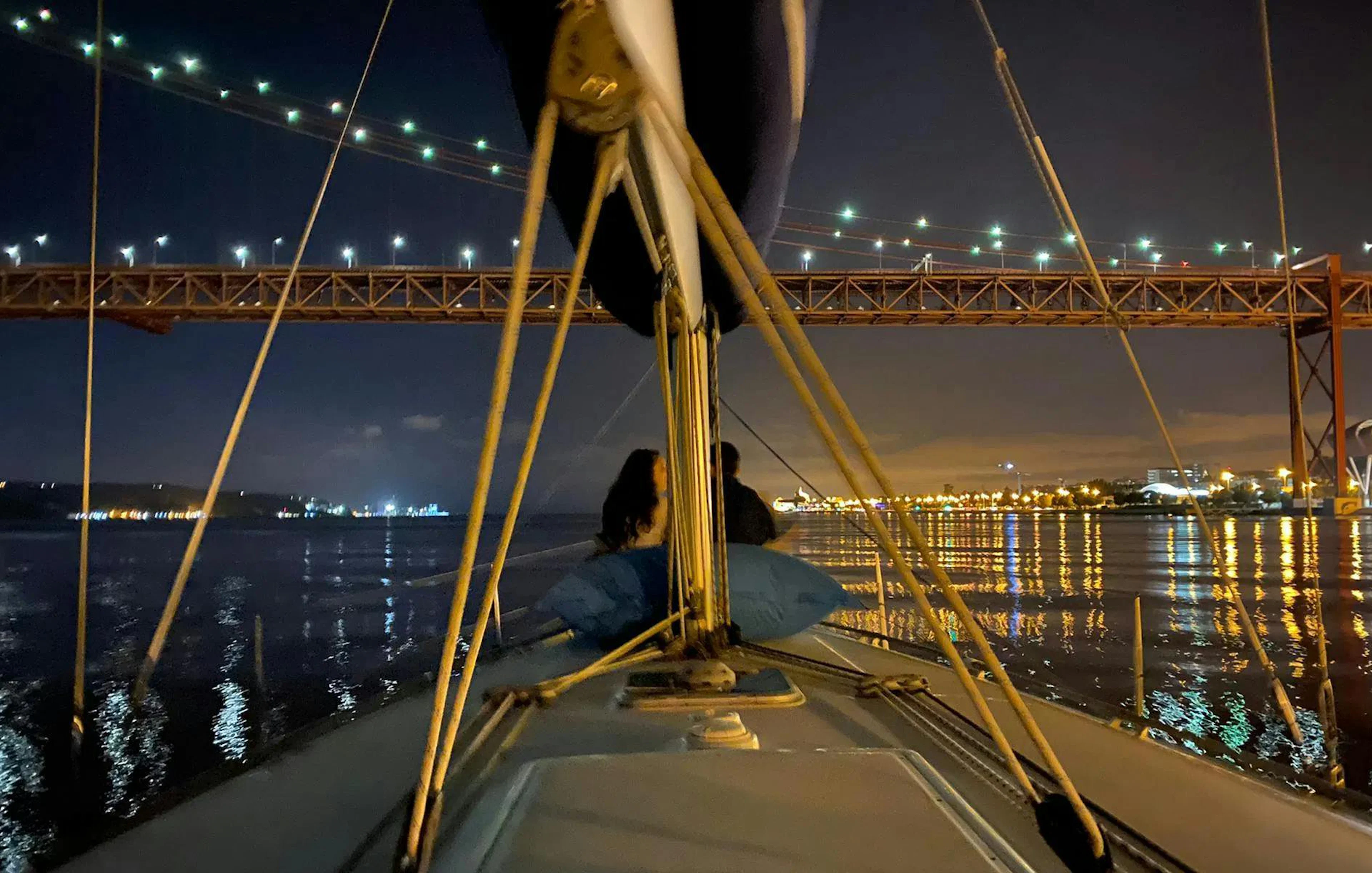 Couple enjoying Lisbon night cruise under illuminated bridge.