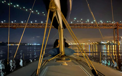 Couple enjoying Lisbon night cruise under illuminated bridge.
