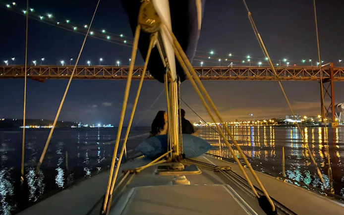 Couple enjoying Lisbon night cruise under illuminated bridge.