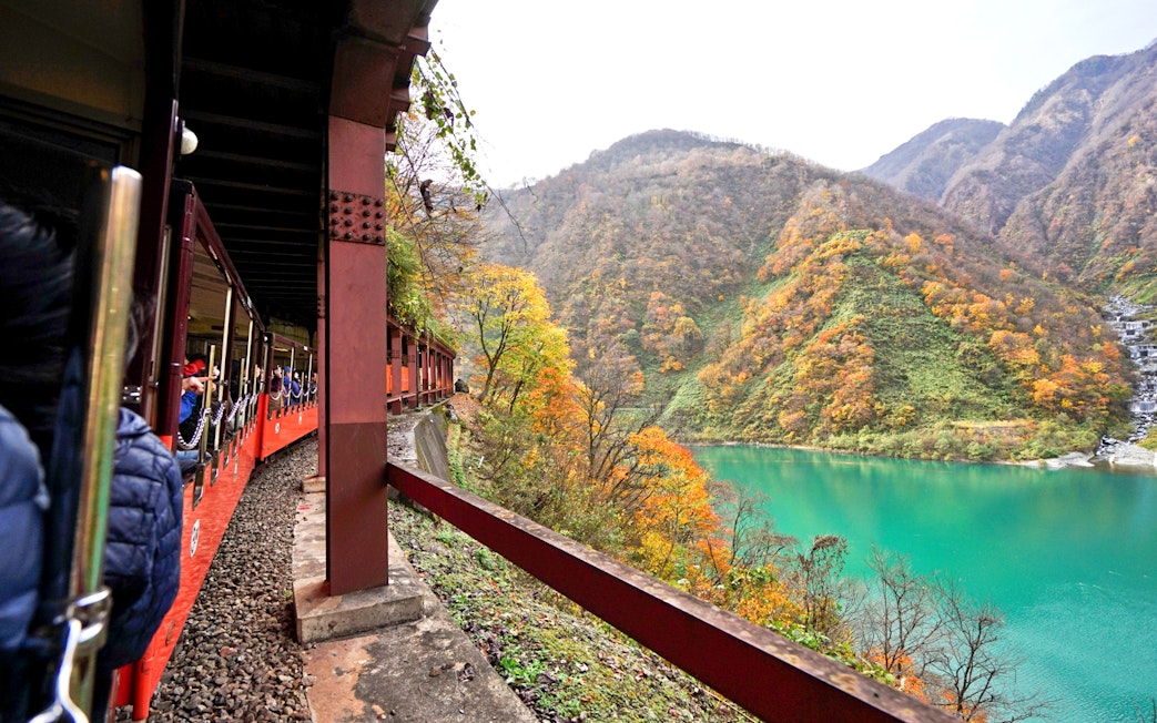 Train journey through Hokuriku mountains with autumn foliage and turquoise river.