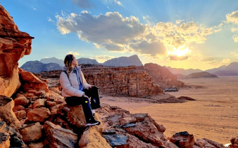 Traveler sitting on rocks at sunset in Wadi Rum desert, Jordan.