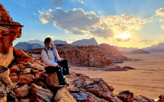 Traveler sitting on rocks at sunset in Wadi Rum desert, Jordan.
