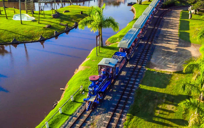 Trenzinho ride at Beto Carrero World passing by a scenic pond and palm trees.