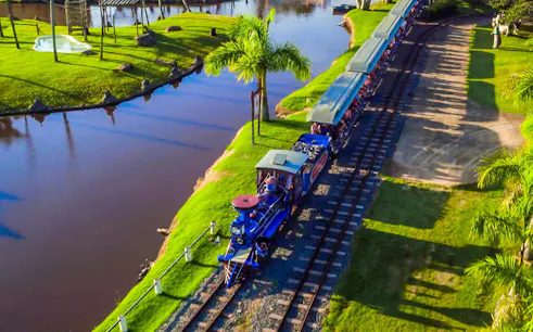Trenzinho ride at Beto Carrero World passing by a scenic pond and palm trees.