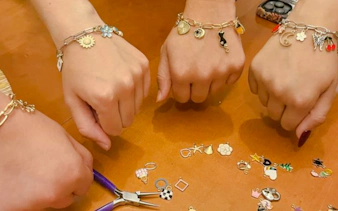 Hands displaying handmade charm bracelets at a jewellery workshop in Essaouira.
