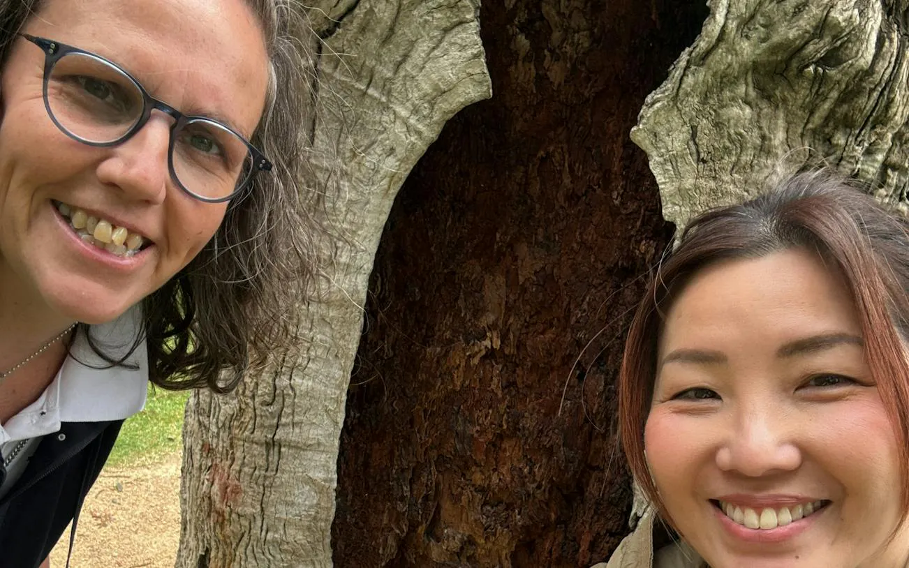 Two people smiling in front of a large tree in Melbourne's Fitzroy Gardens.