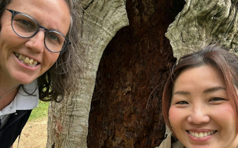 Two people smiling in front of a large tree in Melbourne's Fitzroy Gardens.
