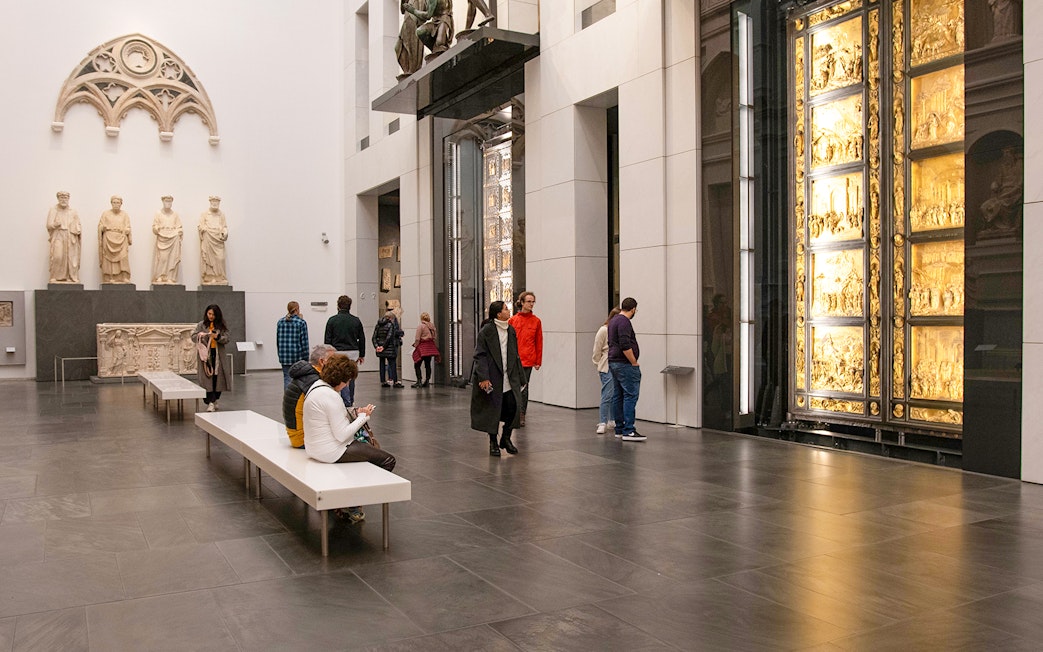 Visitors inside Florence Duomo museum viewing sculptures and the Gates of Paradise.