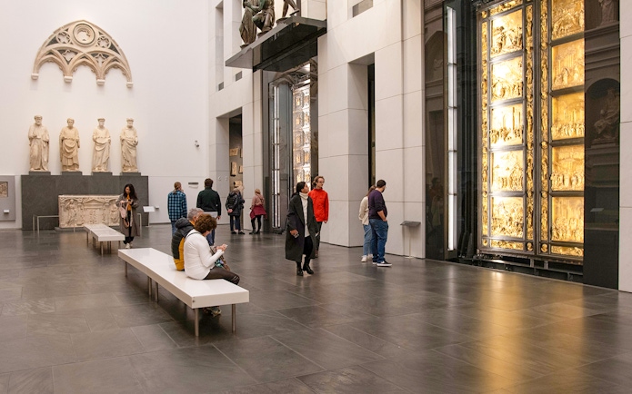 Visitors inside Florence Duomo museum viewing sculptures and the Gates of Paradise.