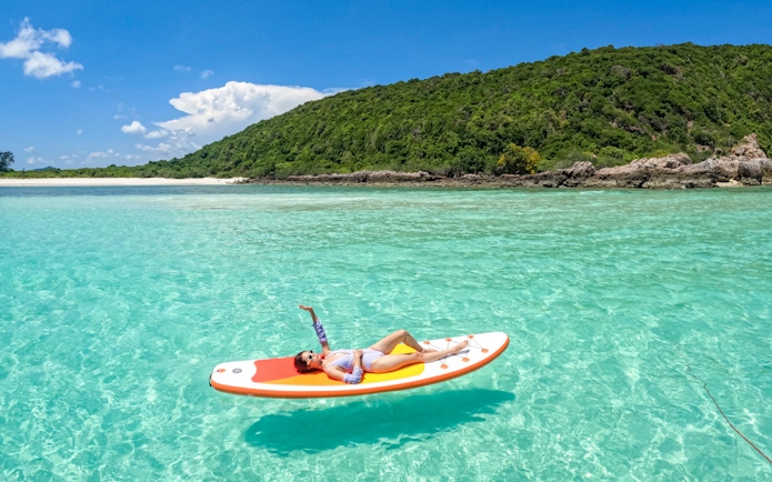 Person relaxing on a paddleboard in clear waters near Nemo Island, Thailand.