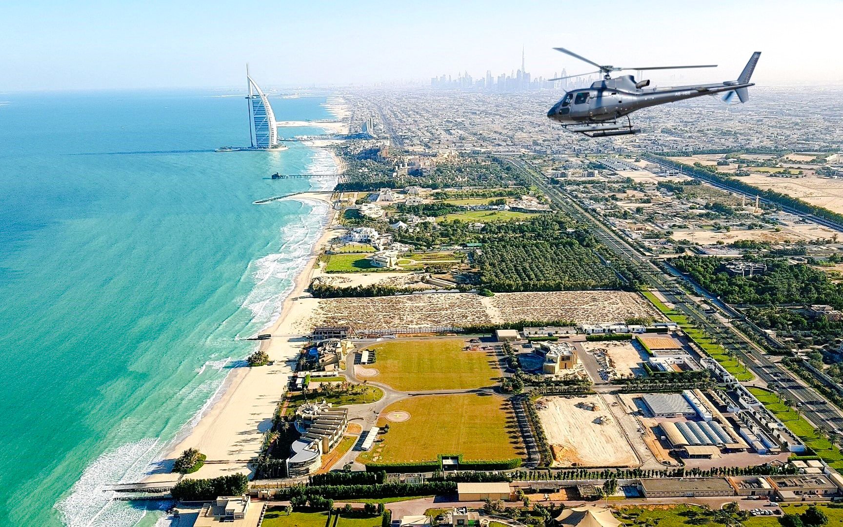 Helicopter flying over Burj Al Arab and Dubai coastline.