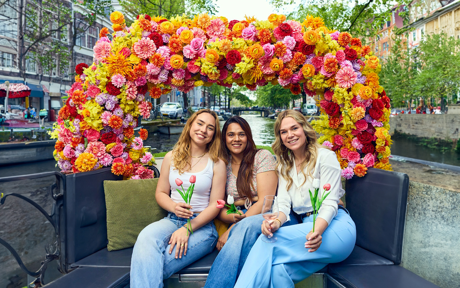 Three people holding tulips on a flower-adorned boat during an Amsterdam canal cruise.