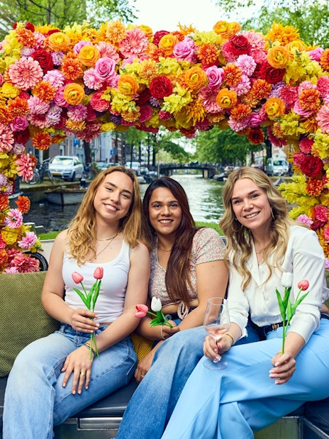 Three people holding tulips on a flower-adorned boat during an Amsterdam canal cruise.
