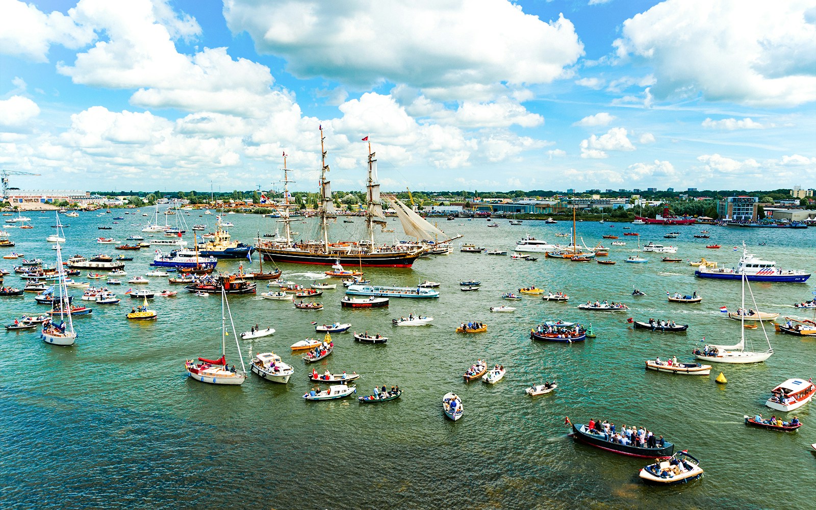 Tall ships and boats in a parade during Sail Amsterdam event.