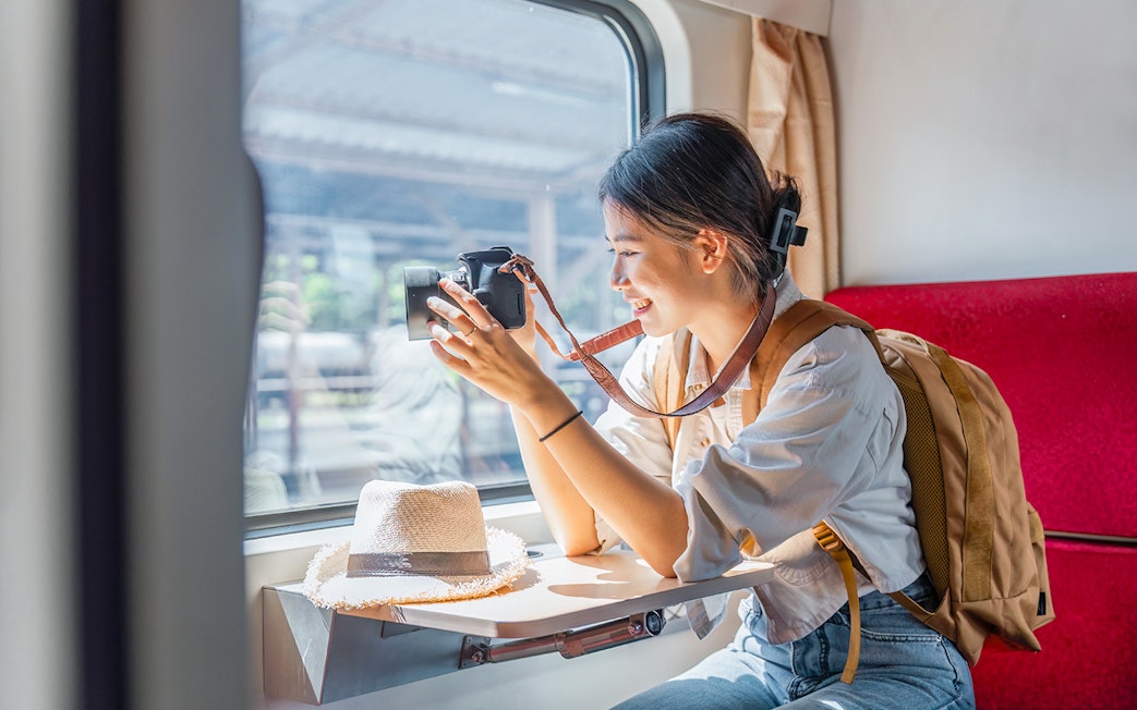 Asian female tourist taking photos from train window with camera.