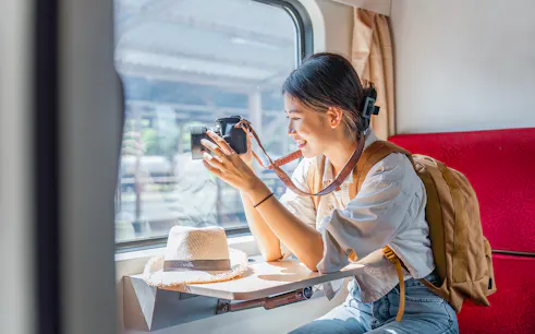 Asian female tourist taking photos from train window with camera.
