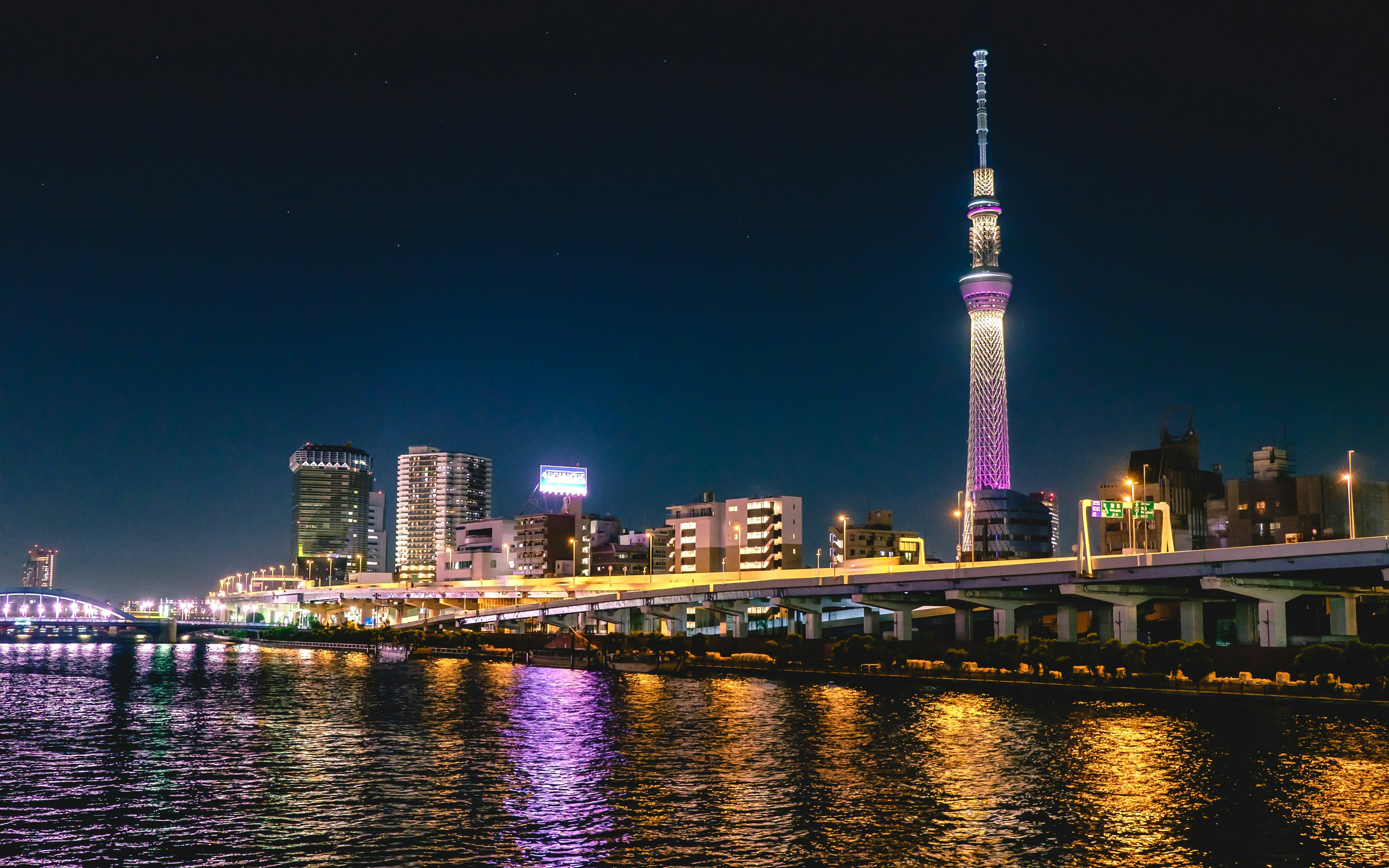 Tokyo cityscape at night with Sumida River reflections and Tokyo Skytree illuminated in the background.