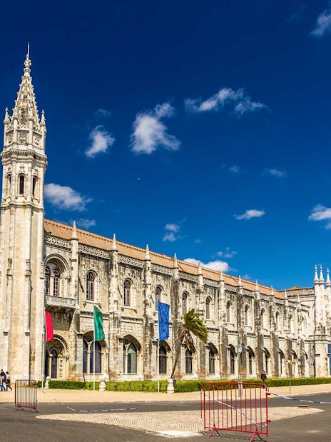 Jerónimos Monastery in Lisbon with blue sky and tourists exploring the site.