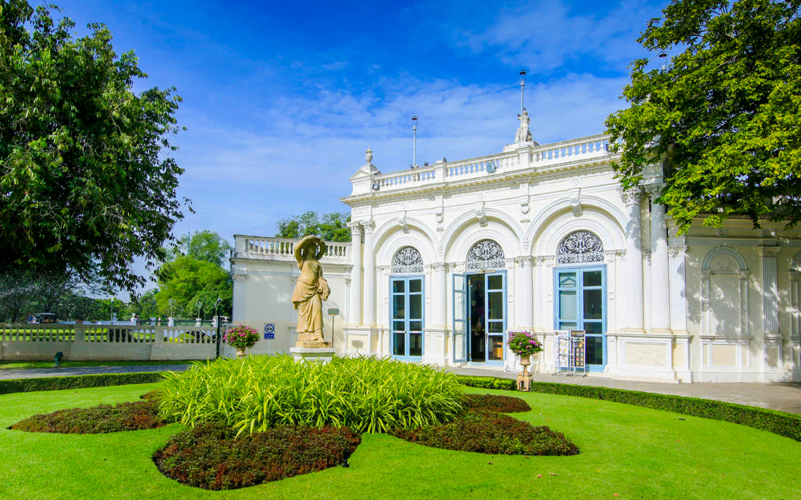 Ayutthaya's Bang Pa-In Palace garden with statue and ornate building.