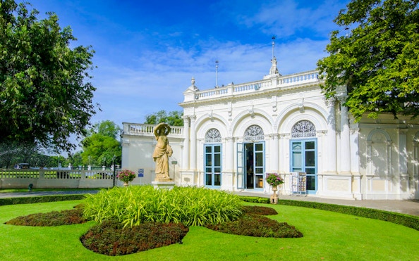Ayutthaya's Bang Pa-In Palace garden with statue and ornate building.