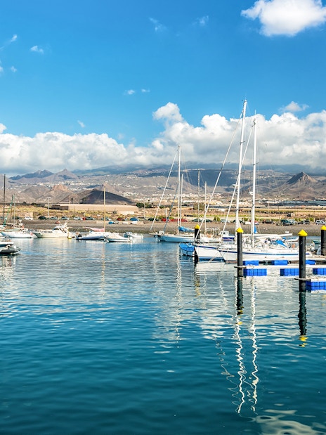 Las Galletas marina with sailboats and mountains in Tenerife under a sunny sky.