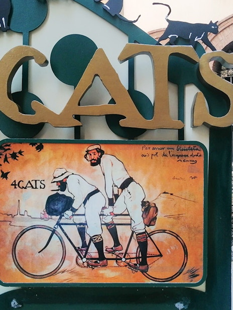 4 Gats sign in Barcelona, featuring artwork of two men on a tandem bicycle, part of Picasso walking tour.