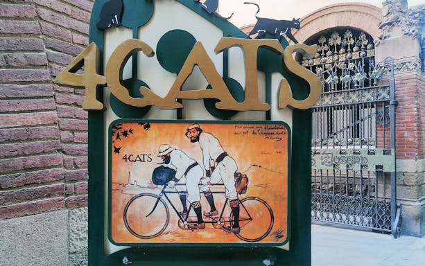 4 Gats sign in Barcelona, featuring artwork of two men on a tandem bicycle, part of Picasso walking tour.