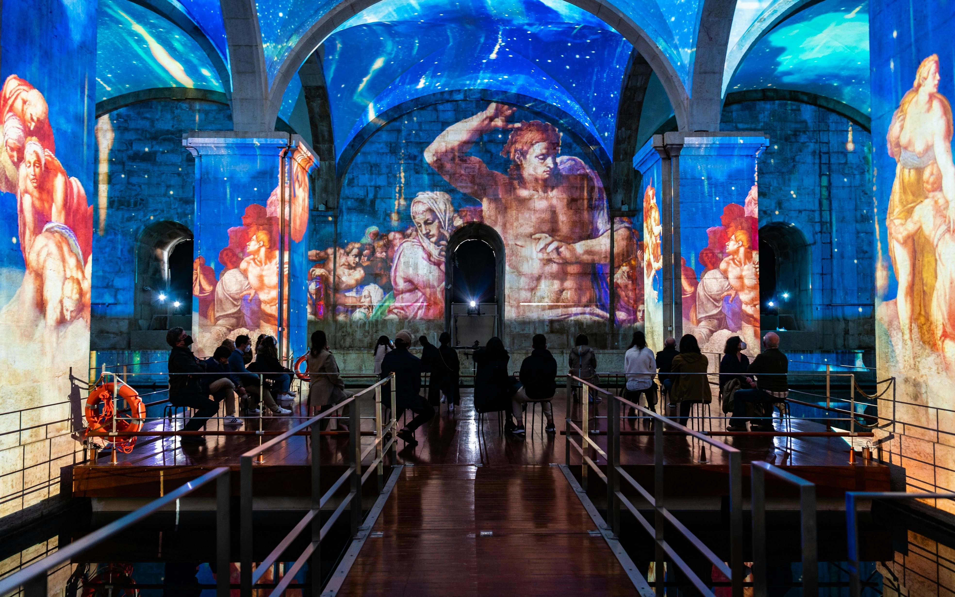 Visitors watching light and sound show at Immersivus Gallery Lisbon with projected art.
