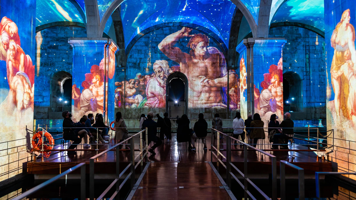 Visitors watching light and sound show at Immersivus Gallery Lisbon with projected art.