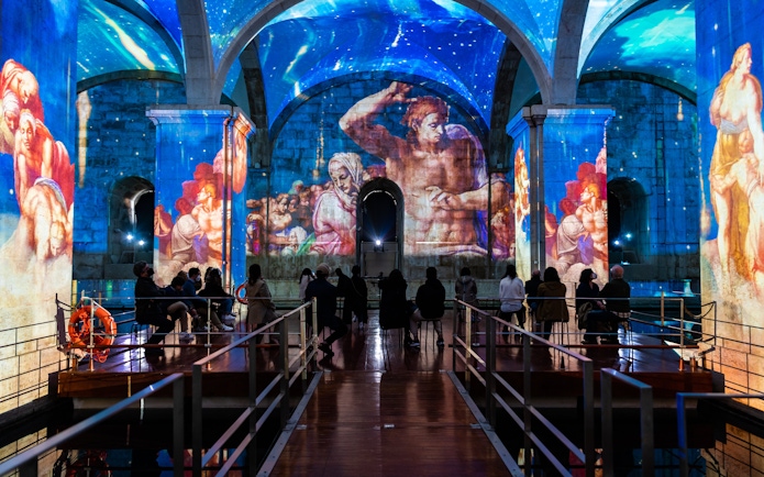 Visitors watching light and sound show at Immersivus Gallery Lisbon with projected art.