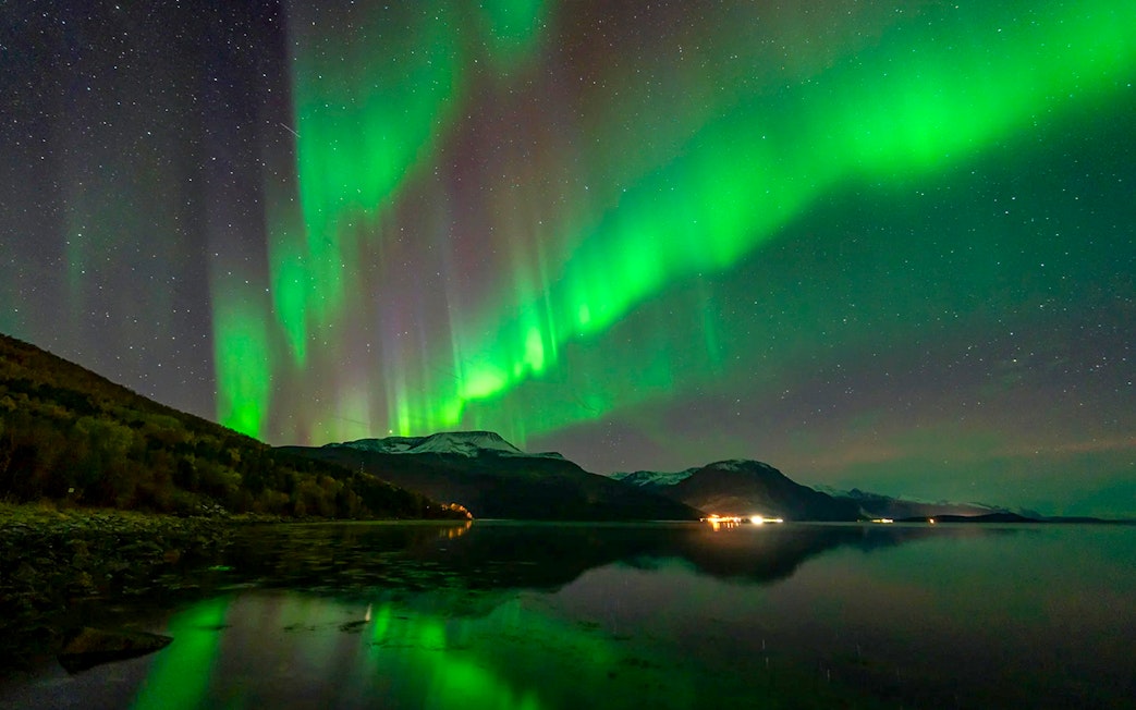 Northern lights over a calm lake during a Chase tour, with mountains in the background.