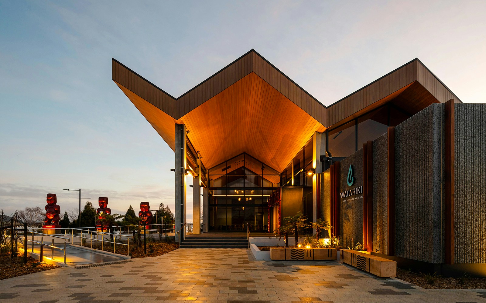 Wai Ariki Hot Springs & Spa entrance with modern architecture and Maori carvings at dusk.