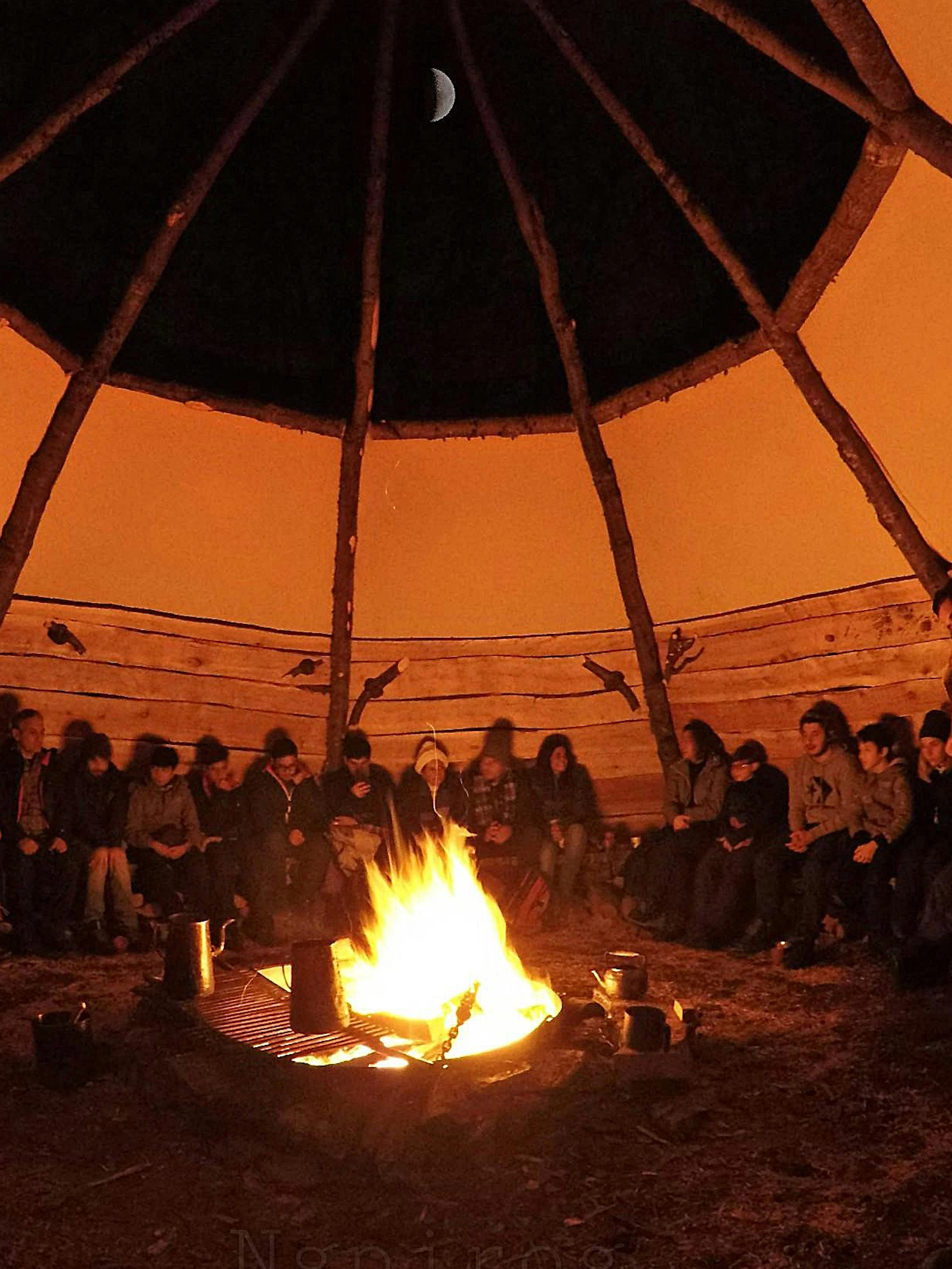 People gathered around a campfire inside a wooden structure during the Snow and Fire Night experience.