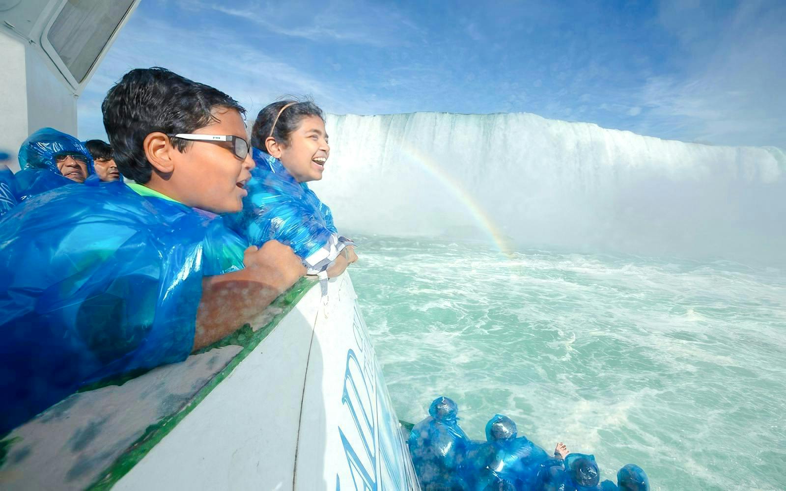 Visitors in blue ponchos on a boat near Niagara Falls USA with a visible rainbow.