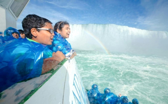 Visitors in blue ponchos on a boat near Niagara Falls USA with a visible rainbow.