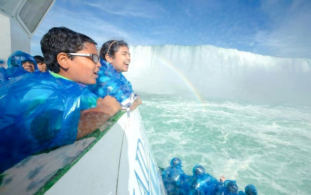 Visitors in blue ponchos on a boat near Niagara Falls USA with a visible rainbow.