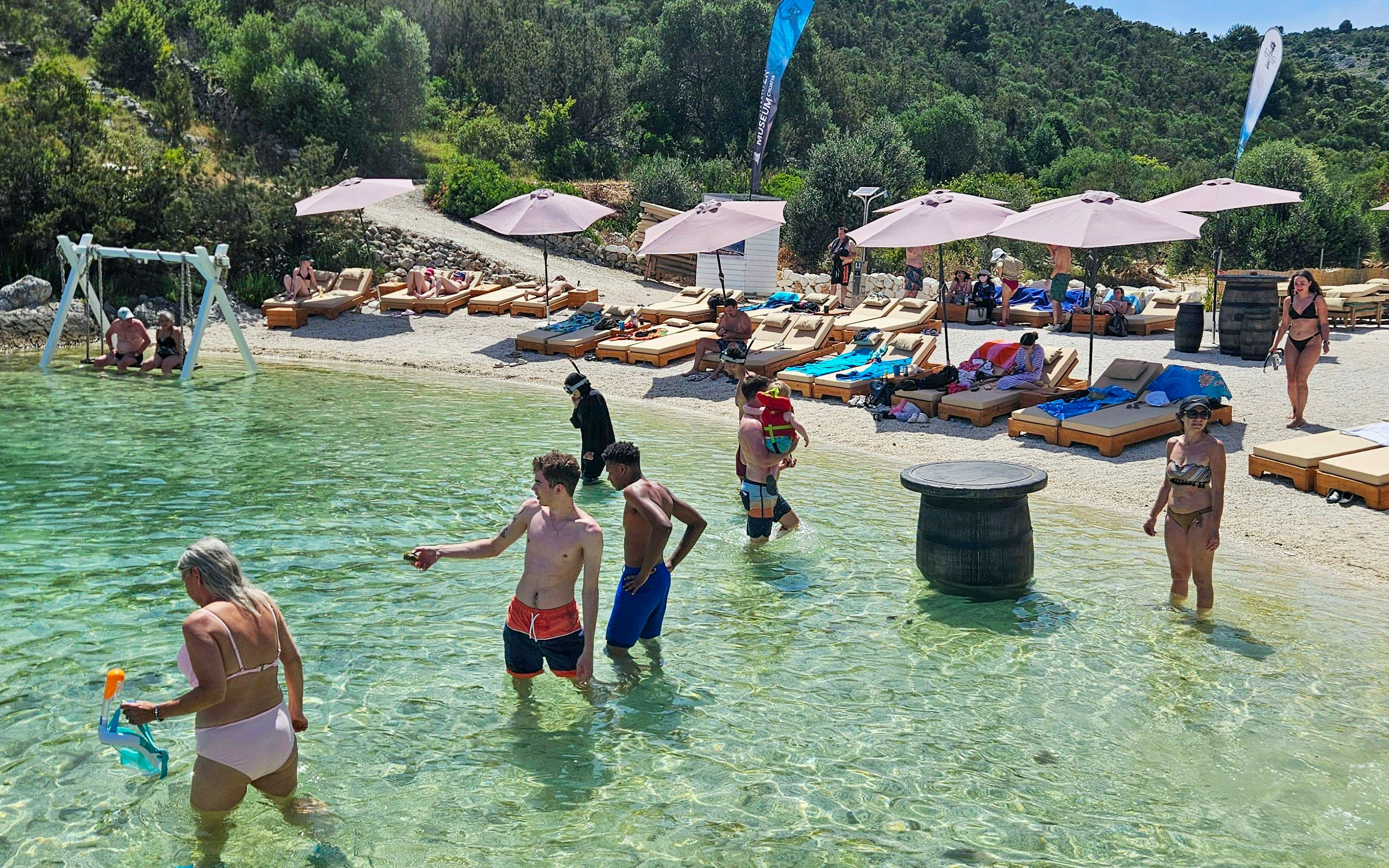 Beachgoers enjoying the water at an exclusive beach resort with sun loungers and umbrellas.