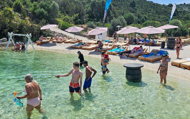 Beachgoers enjoying the water at an exclusive beach resort with sun loungers and umbrellas.