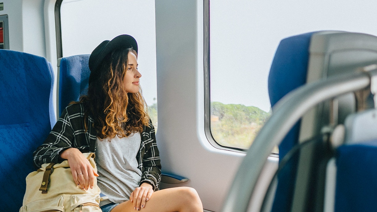 Girl with hat and backpack sitting on a train, looking out the window.