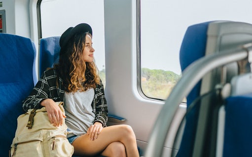 Girl with hat and backpack sitting on a train, looking out the window.