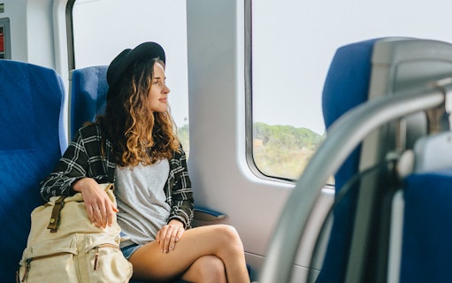 Girl with hat and backpack sitting on a train, looking out the window.