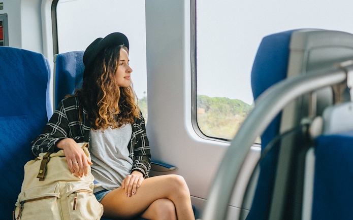 Girl with hat and backpack sitting on a train, looking out the window.