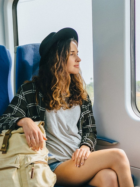 Girl with hat and backpack sitting on a train, looking out the window.