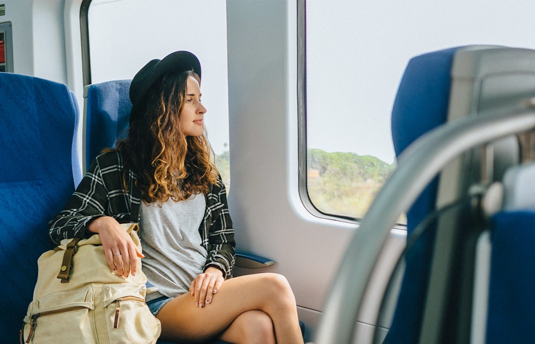 Girl with hat and backpack sitting on a train, looking out the window.