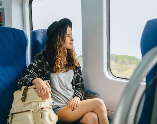 Girl with hat and backpack sitting on a train, looking out the window.