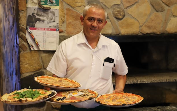 Server presenting assorted pizzas in Trastevere pizzeria during guided food tour.