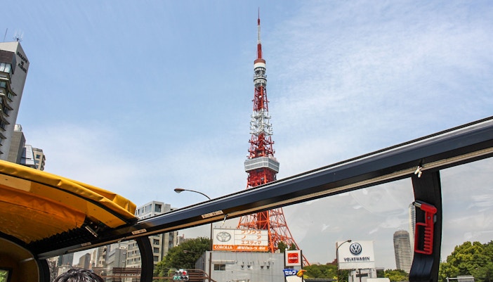 Tourists enjoying a HOHO Bus tour in Tokyo, Japan, with a view of the city's skyline and landmarks from the open-top bus